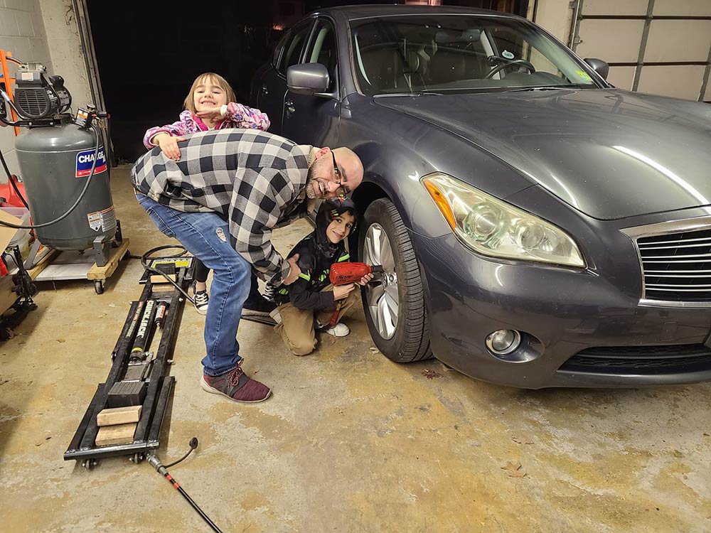 Children help a mechanic work on a car.